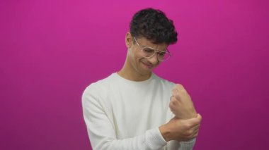 Genç İspanyol bir adam pembe bir stüdyoda yüzünü buruşturuyor ve bileğini sıkıyor..