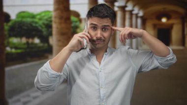 Genç İspanyol bir adam cep telefonuyla işaret eder, eski bir üniversitenin önünde dikilirken, inanmadığını ya da hayal kırıklığına uğradığını söyler..