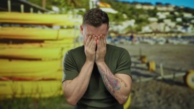 Deniz kenarında yüzüne dokunan dövmeli genç adam plaj geçmişi bulanık, yaz gününü düşünüyor..