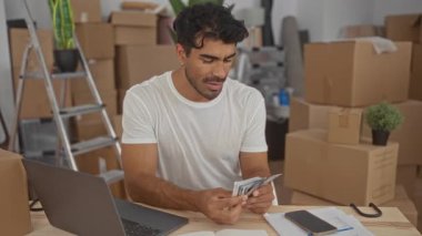 Adam, binadaki karton kutular arasında dizüstü bilgisayarla ahşap masada elleri ile nakit sayıyor; konsantrasyon.