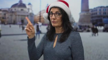 Kırmızı Noel Baba şapkalı kadın, Vatikan Meydanı 'ndaki bir binanın ön cephesinin yanındaki izleyiciyi işaret ediyor..