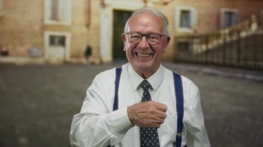 Eski üniversite binasının dışındaki kameraya bakarken güvenle gülümseyen takım elbiseli kıdemli adam..