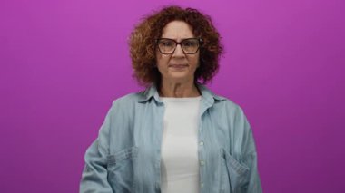 Canlı pembe arka planda yüzünü kapatan kadın rahat bir kot gömlek giyiyor. Ayrı bir ortamda oyuncu utangaçlığı ifade ediyor..