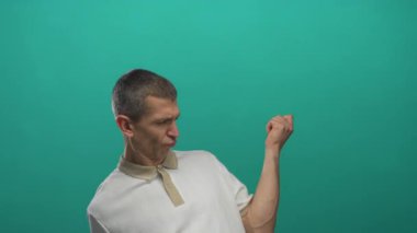 Yeşil arka planda gitarı anlamlı hareketlerle taklit eden adam.