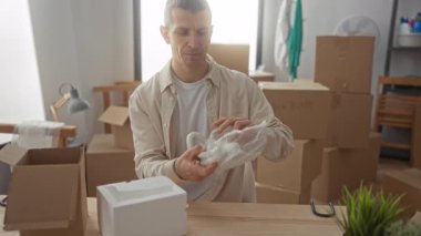 Parlak bir oturma odasındaki kutularla çevrili yeni bir evde bavulları boşaltan adam modern bir dairede eşyaları dikkatlice düzenliyor..
