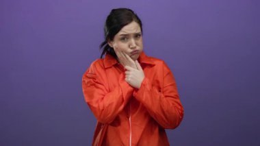 Turuncu hapishane tulumu giymiş, acı içinde yüzünü buruşturan, mor arka planda çenesini tutan bir kadın diş ağrısını hapsettiğini gösteriyor..