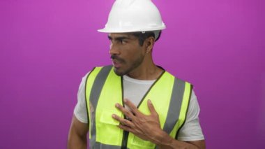 Beyaz kasketli ve yansıtıcı yelek giyen İspanyol mühendis stüdyoda göğsüne dokunuyor..