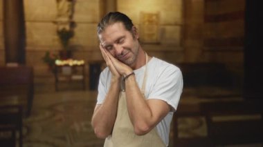 Önlük giyen adam elleri kapalı ve kilise binasında nazikçe gülümsüyor. Huzur..