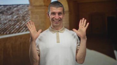 Gülümseyen adam, tarihi üniversite kampüsünde güneşli bir günün keyfini çıkarıyor. Güzel kemerli koridorun altında ellerini kaldırarak klasik mimari ve eğlence havasını sergiliyor..