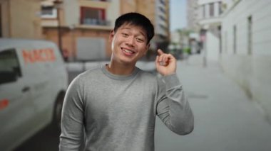 Bir fikir jesti ile genç adam şehir caddesinde duruyor, açık şehir ortamında yaratıcılık ve pozitifliği ifade ediyor, günlük giysiler ve neşeli bir ruh hali sergiliyor..