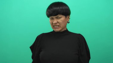 İzole edilmiş yeşil arka plana, siyah süveter ve küpe giyen ve stüdyo ortamında duygularını gösteren kadınlara karşı tiksinti besliyordu..