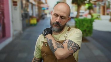 Şehir caddesinde sakallı bir adam, önlük ve eldiven giyiyor, güneşli bir günde, şehirde yorgunluk gösteriyor..