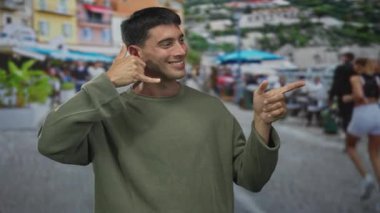 Yeşil eşofman giyen genç İspanyol adam sol eliyle işaret ediyor ve sağ eliyle sokakta işaret ediyor; bağlantı.