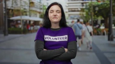 Bulanık insanların ve kentsel çevrenin geçmişine sahip hareketli caddede kameraya güvenle bakan gönüllü tişört giyen bir kadın..