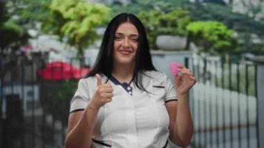 Çevresel farkındalığı vurgulayan canlı kentsel bir ortamda, canlı bir şehir arka planında pembe bir adet bardağını tutan bir kadın gülümsüyor.