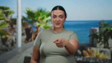 Bana işaret eden bir kadın, yeşil gömlekli, gülümseyen, açık hava, tropikal ortam, gündüz kuşağı, neşeli, rahat atmosfer..