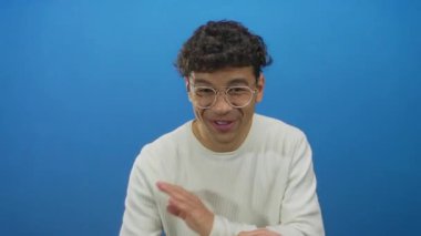 Stüdyoda gülümserken işaret eden gözlüklü İspanyol adam canlı mavi arka plana karşı; neşe.