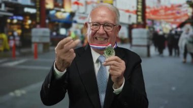 Üst düzey takım elbiseli adam, kalabalık caddede elinde gümüş madalyayla orta parmağıyla saldırgan hareketler yapıyor..