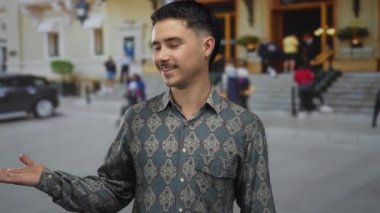 Genç İspanyol adam hareketli bir şehir caddesinde dikilirken elini uzatıyor binalar ve arabalarla dolu, canlı bir şehir atmosferini yakalıyor..