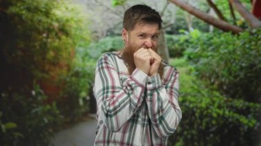 Ekose gömlek giyen uzun kızıl sakallı bir adam yeşil yapraklarla çevrili orman yolunda gözlerini kısarak el ele tutuşuyor..