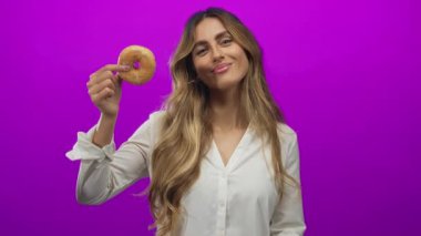 Stüdyoda donutu işaret eden genç sarışın kadın; oyun tutkusu cazibe cazibesi.