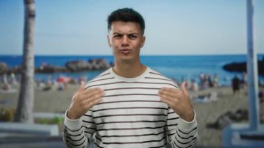 Yakışıklı genç adam çizgili gömleğiyle canlı bir sahil sahilinde arka planda palmiye ağaçları ve okyanuslar olan açık havada sıradan bir yaz havası yayıyor..