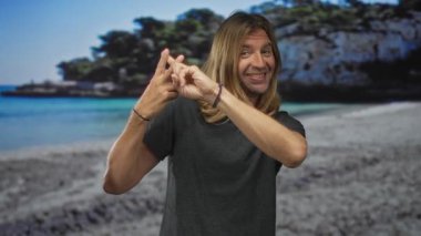 Güneşli sahil sahilinde hashtag hareketi yaparken gülümseyen uzun sarı saçlı bir adam..