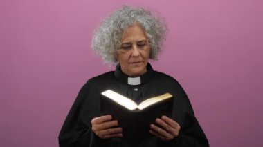 Gri saçlı kadın rahip pembe arka planda İncil okuyor..