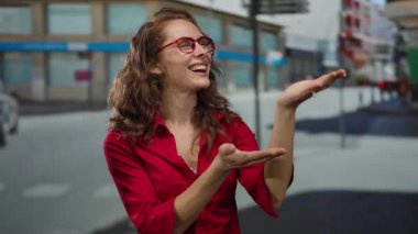 Şehirli bir kadın, açık havada kırmızı tişörtlü, güler yüzlü güneşli bir günde arka planda geziyor..