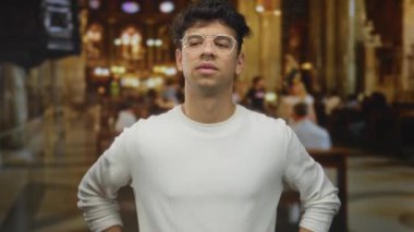 Çapraz kollu beyaz kazaklı bir adam kilisenin içinde vitray pencerelerin altında dikiliyor ve reddedildiğini gösteriyor..