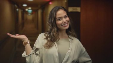 Gülümseyen kadın, aydınlık modern otel binasında kol saatini göstererek el ele uzanır; neşe içinde karşılanır.