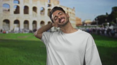 Roma kolezyum binasının önünde boynuna dokunan adam beyaz tişört giyiyor, tatil tatili neşe içinde..