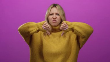 Onaylamadığını belirten bir kadın, parlak pembe duvarın önünde, hoş sarı süveter giyen, baş parmakları havada bir jest yapıyor.