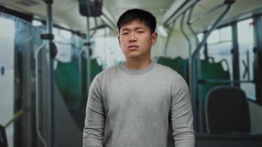 Otobüsteki gri kazaklı genç adam, kapalı arka plan ve bulanık yeşil koltuklardan rahatsız olmuş görünüyor. Toplu taşıma araçlarında günlük gidip gelişleri gösteriyor.