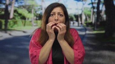 Orta yaşlı İspanyol kadın parkta kaldırım boyunca yeşil ağaçların yanında yanağına bastırıyor, korku..