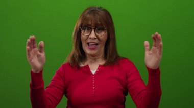 Kırmızı tişörtlü İspanyol son sınıf öğrencisi elleri ile büyük jest yapıyor, canlı yeşil duvar arkaplanına gülümsüyor, neşe ve sıcaklık taşıyor..