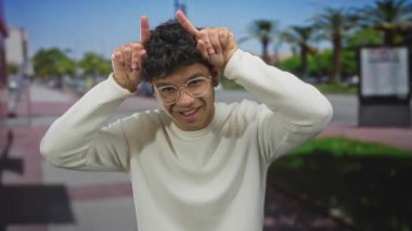 Gözlüklü genç İspanyol adam boynuz hareketi yapıyor. Parmakları sokakta, palmiye ağaçlarıyla. Eğlenceliymiş..