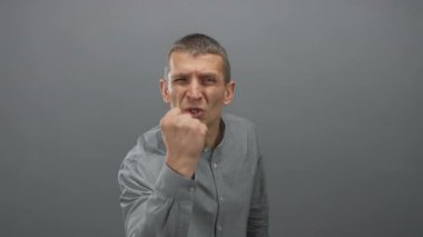 Öfkesini yumruğuyla dışlanmış gri duvar arkaplanına karşı gösteren bir adam, hayal kırıklığı ve öfke gösteriyor..