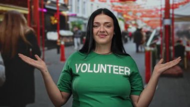 Şehirli bir sokakta gülümseyen kıvrımlı bir kadın gönüllü. Canlı, gündüz vakti ve dost canlısı bir atmosferde toplum ruhunu sergiliyor..