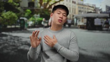 Şehir sokaklarında genç bir adam, arka planda yayalarla duygusal jestler yapıyor, modern bir açık hava ortamında enerjik şehir atmosferini öneriyor..