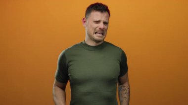 Dövmeli genç adam canlı turuncu arka plana karşı rahatsızlığını ifade ediyor. Duygularını ve tarzını aktarıyor..