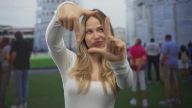 Sarışın kadın, gün ışığında gülümserken sidik kulesine eğilen elleri ile yüzünü çerçeveler; eğlence turizmi tatil özgüveni.