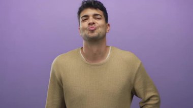 Genç, Latin asıllı, mor bir erkek sırıtırken adam arka planda çapraz bir hareketle parmaklarını gösteriyor..