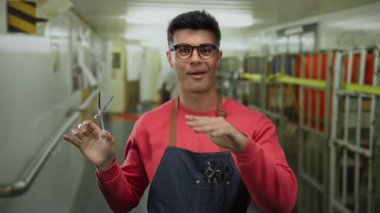 Bir yolcu gemisinde gözlüklü genç bir adam koridorda durduğu sırada elinde makasla güvenle bir önlük tutarak modern ve dinamik bir yaşam tarzını ön plana çıkarıyor..