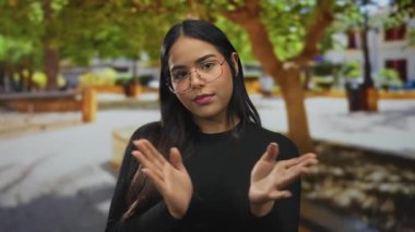 Parkta el çırpan elleri olan bir kadın, genç Latin kökenli ve açık havada yeşil ağaçların arasında, sıkılmış görünüyor..