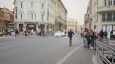 Roma caddesinde, bulutlu gökyüzü altında tarihi binalar ve arabalarla bulanık insanlar..