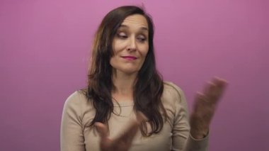 Bej kazak giyen genç İspanyol kadın pembe duvar stüdyosunda olumlu bir jest sergiliyor..