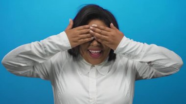 Gözleri kapalı gülen ve sonra kollarını kaldıran, mavi arka planda gözlük ve beyaz gömlek giyen, neşeli ruh hali gösteren bir kadın..