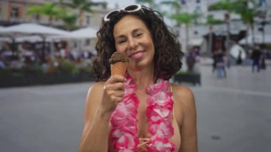 Lei 'li orta yaşlı İspanyol kadın güneşli bir caddede hareketli bir teras restoranında çikolatalı dondurmayı seviyor, yaz havasını ve neşesini yakalıyor..