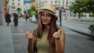 Parkta parktaki genç bir kadın, güneşli bir günde şapkasını takmış güneşli bir havada gülümseyen ve şehir ortamında yaz atmosferini yansıtan paralarla el kol geziyor..